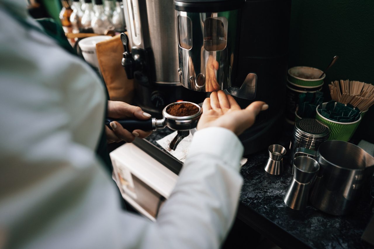 Manos de barista preparan café molido junto al equipo de la barra.